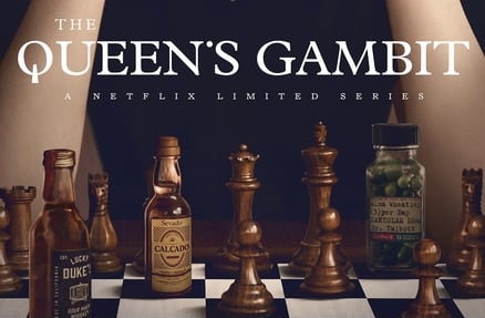 chess board with chess pieces and mini liquor bottle on it. Series tile: The Queen's Gambit across the top of the picture