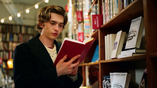 Teen boy standing in a bookshop reading a notebook