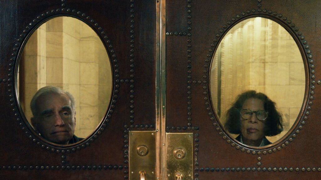 a double door with a oval window on each. a man looking through one window and a woman looking through the other