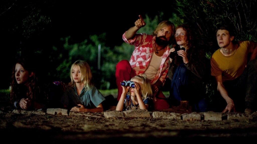 A man, sitting in the woods on a dark night, pointing out stars to his six children