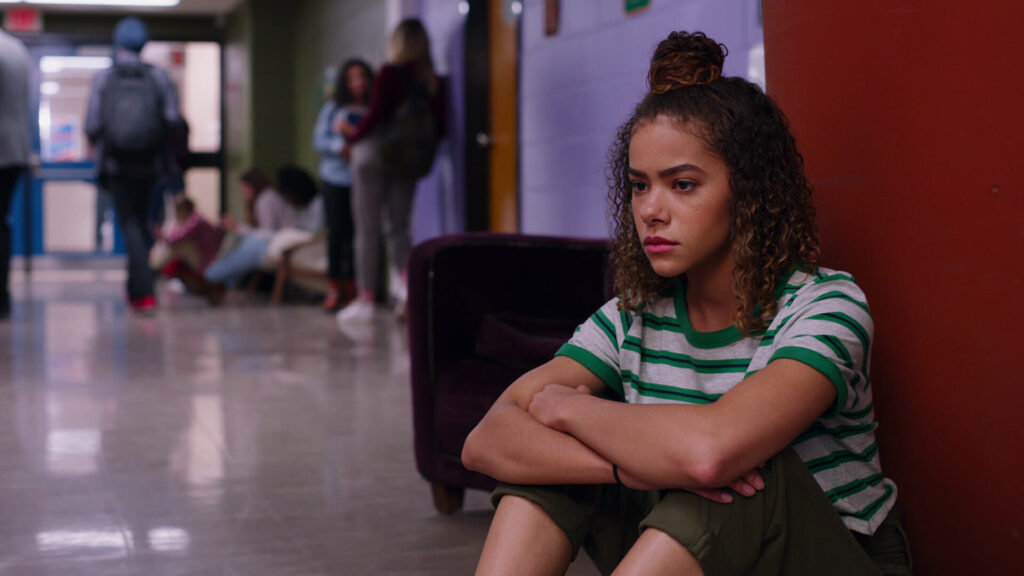 A teen girl, sitting by herself on the floor of a school hallway