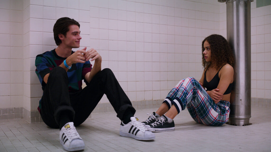 A teen boy and a teen girl sitting on the floor of a bathroom