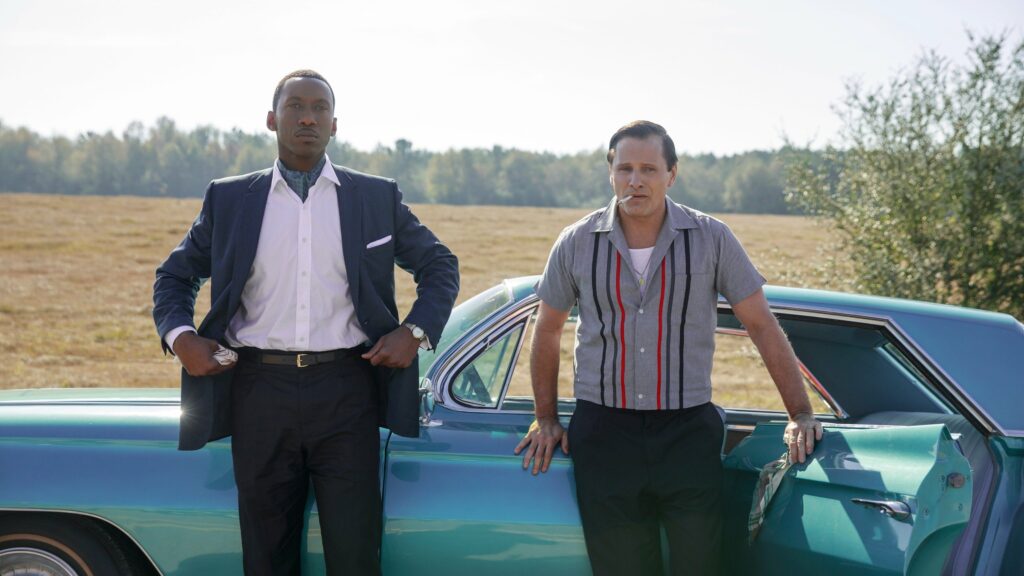 A black man and a white man leaning against a car