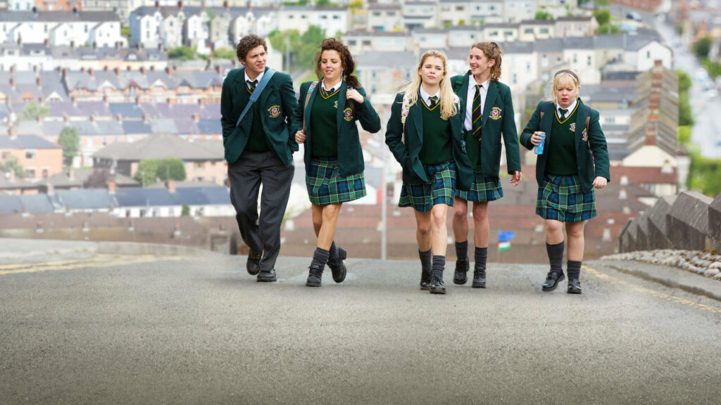 Four teen girls and a teen boy, wearing school uniforms walking down a street