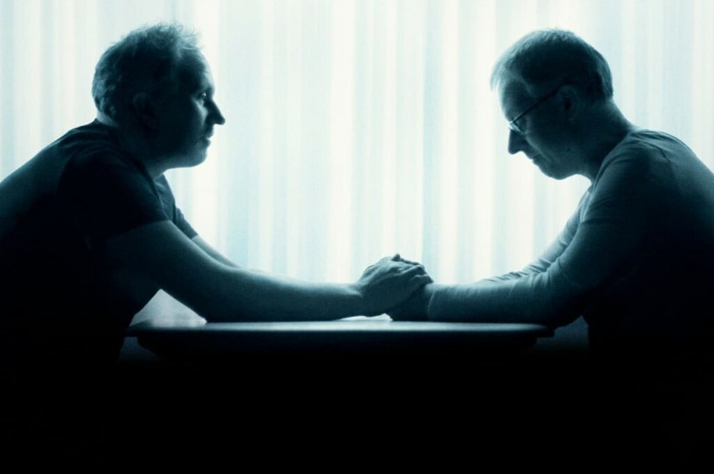 two brothers, sitting across the table from each other, holding hands