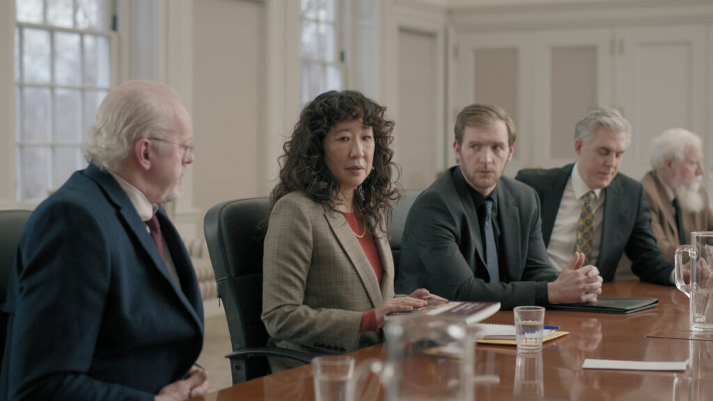 A lone woman siting at a boardroom table with several men